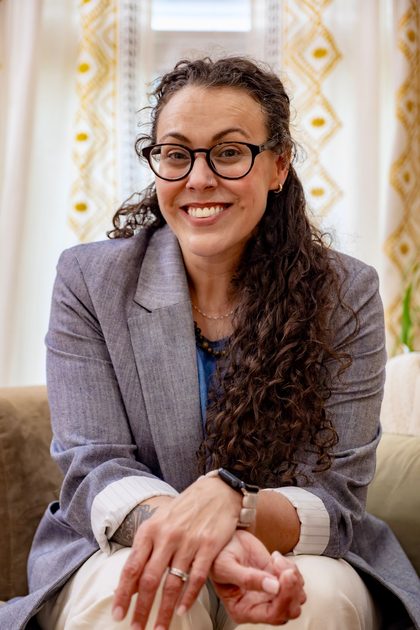 Tiffany Acuff, therapist at Whole Self Counseling, seated with hands folded in front of patterned curtains