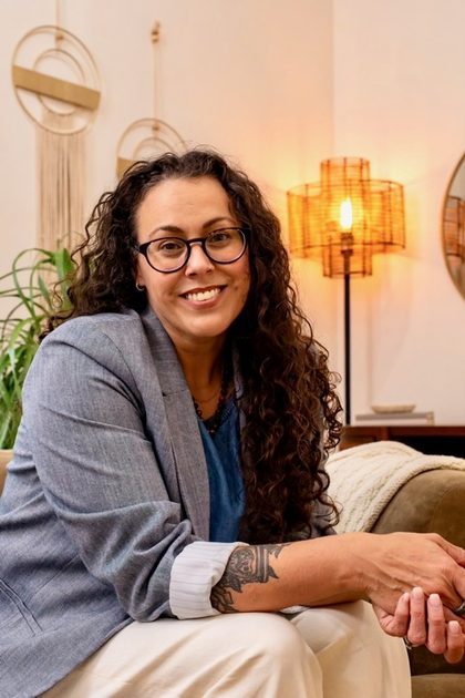 Tiffany Acuff, therapist at Whole Self Counseling, seated on a couch wearing glasses with warm light behind her